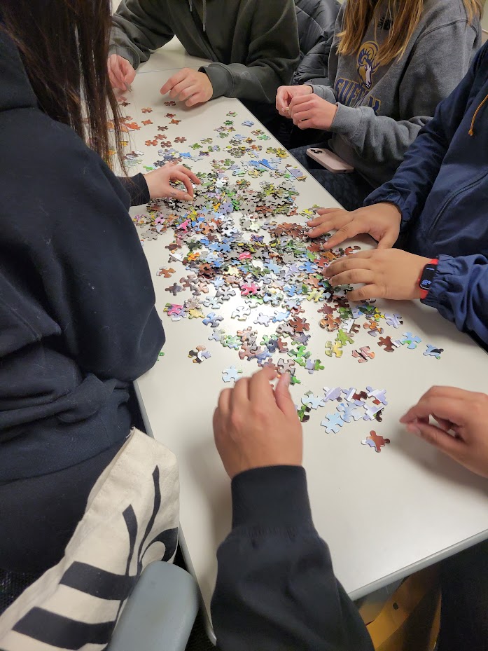 A photo of students sitting around a table assembling pieces of a puzzle.