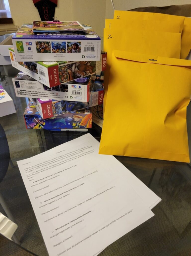 A photo of bulky orange paper packages, stacked puzzle boxes, and printed assignment guidelines.